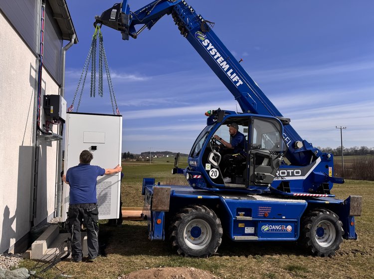 Mitarbeiter von Elektro Kessler stellen mit einem Kran einen großem PV-Speicher auf.