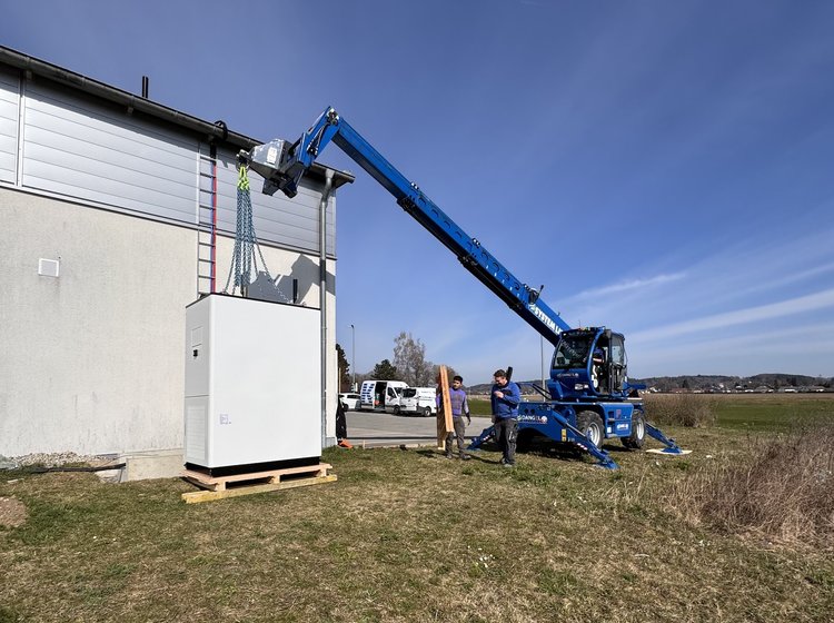 Elektro Kessler montiert mit einem blauen Kran einen PV-Speicher neben einem Gebäude.