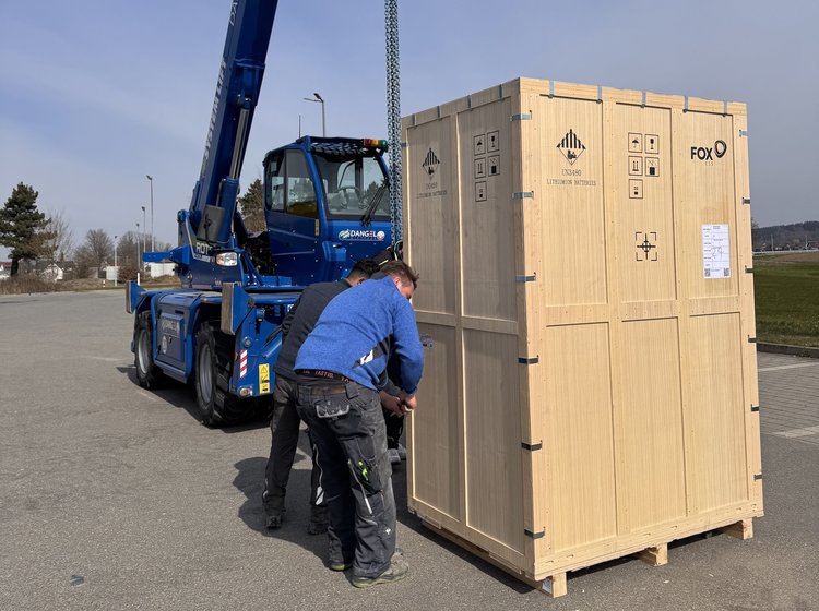 Zwei Mitarbeiter von Elektro Kessler transportieren einen großen PV-Speicher mit einer Holzbox an einem Kran.