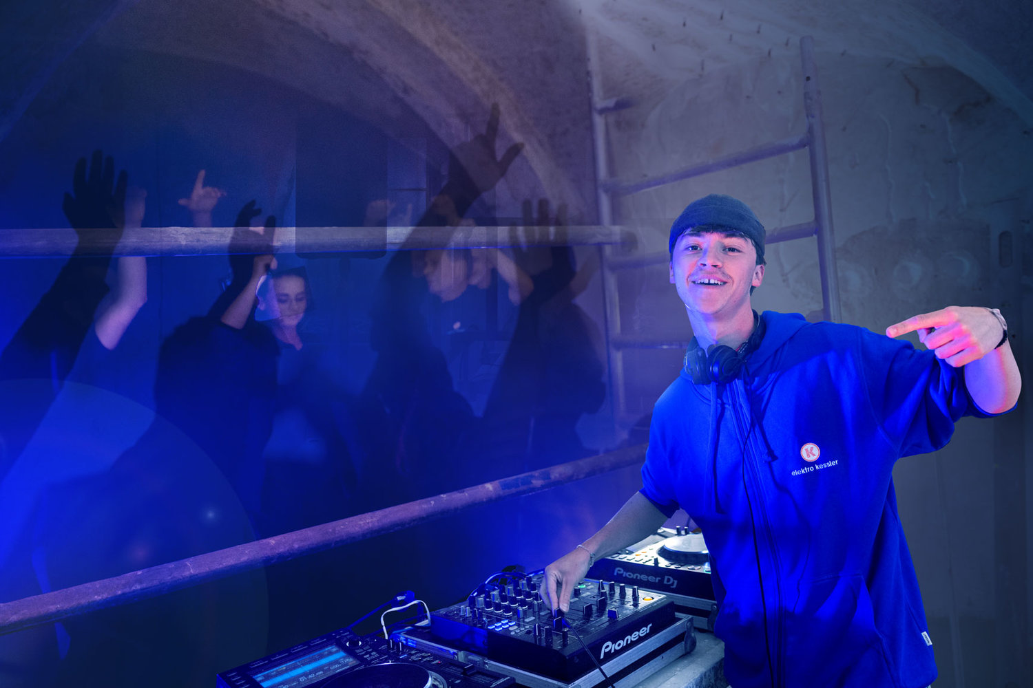 DJ Paul Amschlinger steht am Mischpult, im Hintergrund feiernde Menschen